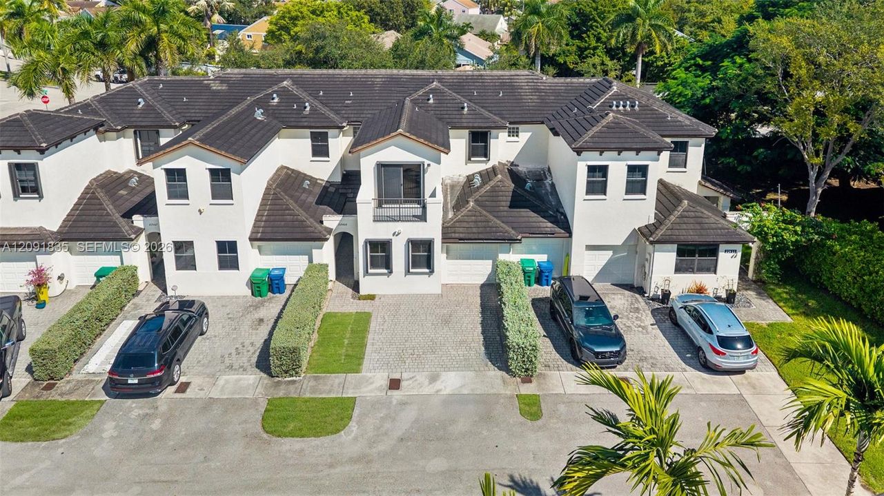 Multi-unit structure featuring a light-toned stucco exterior, dark shingle roof, paved private driveways, and upper-level balconies