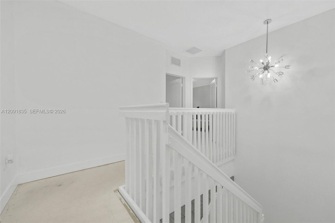 White stairwell featuring a wood handrail, vertical balusters, and a starburst chandelier