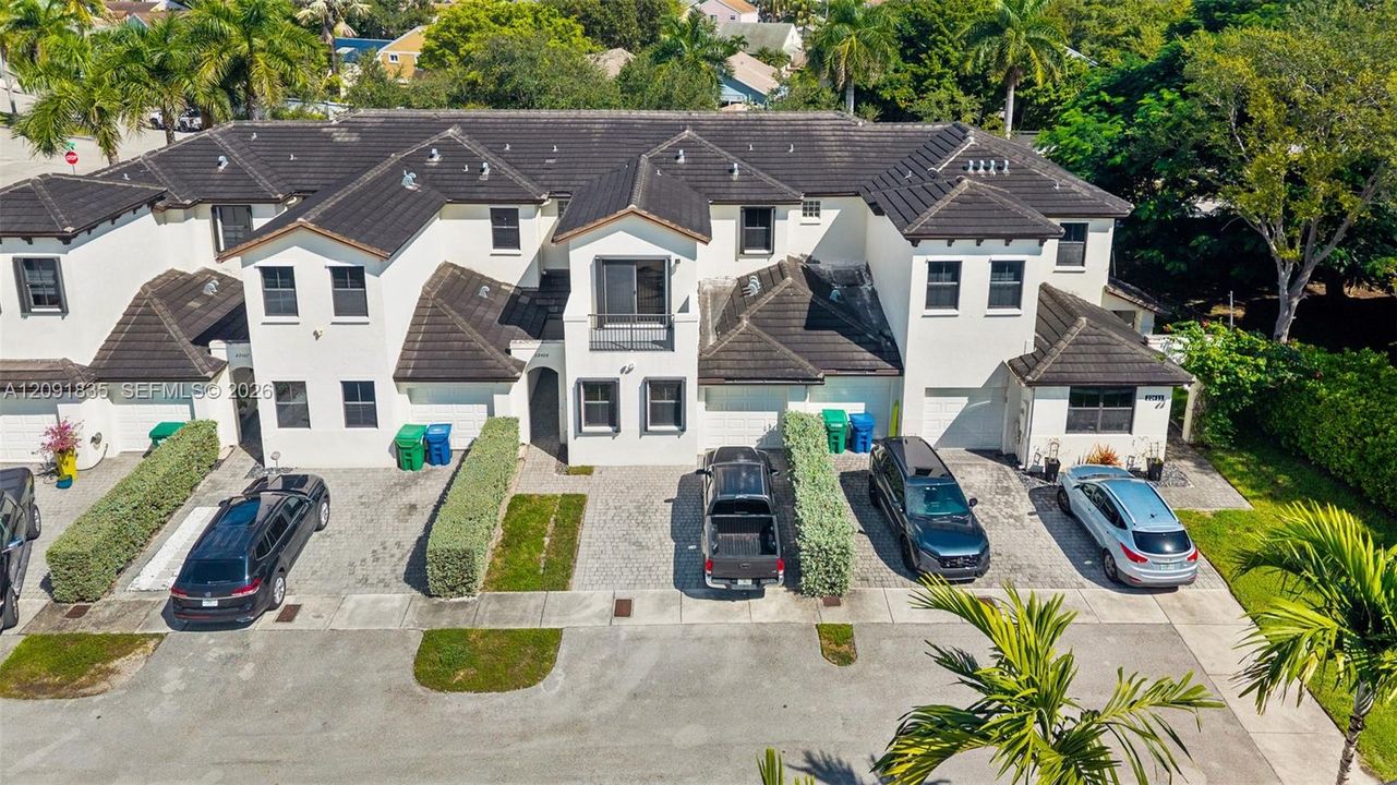 Multi-unit residential structure with stucco exterior, dark tile roofing, individual attached garages, and private balconies