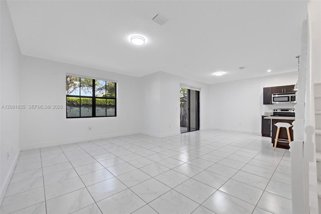 Open-concept interior featuring large-format tile flooring, recessed lighting, expansive windows with dark frames, and kitchen cabinetry with integrated stainless steel appliances