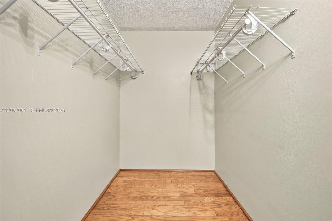 Storage space featuring dual-level white wire shelving and wood-finish flooring