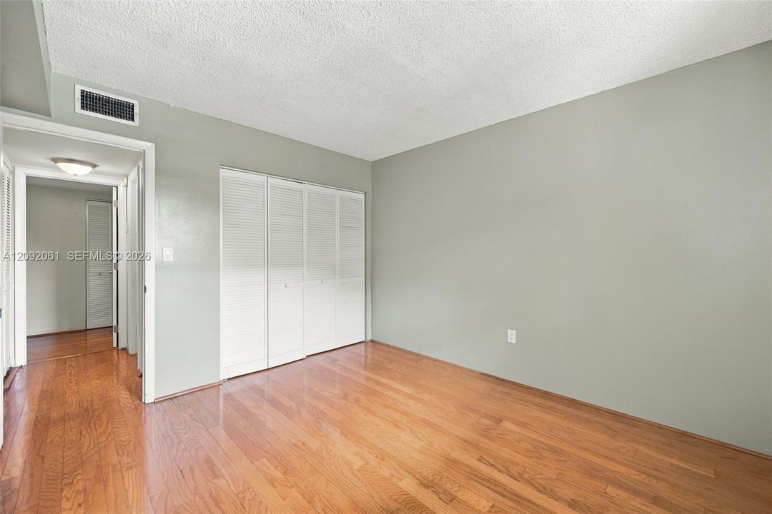 Room interior featuring wood-finish flooring, neutral-toned walls, and a multi-panel louvered closet door