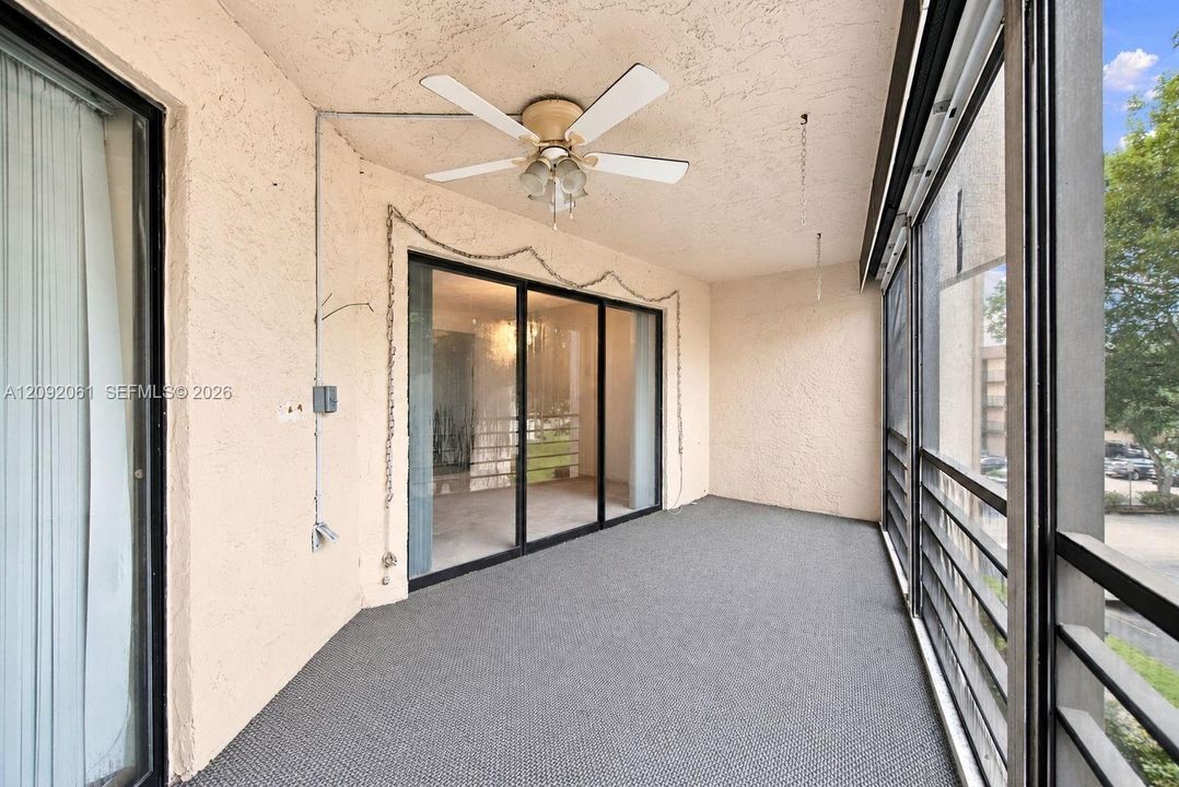 Screened-in balcony featuring stucco walls, a ceiling fan with integrated lighting, metal railings, and sliding glass entry doors