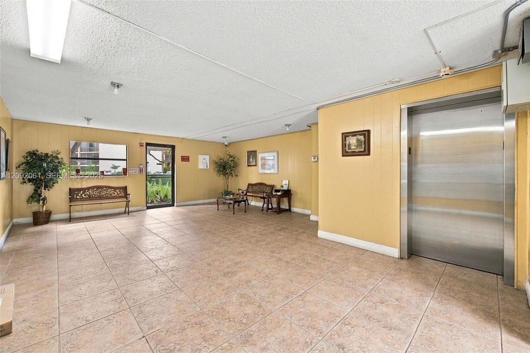 Common area lobby featuring tile flooring, panel-accented walls, and a stainless steel elevator