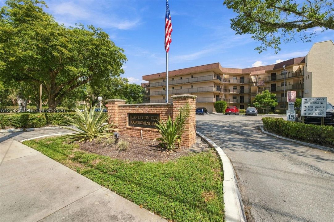 Community entrance featuring a brick monument sign, mature landscaping, and asphalt driveway