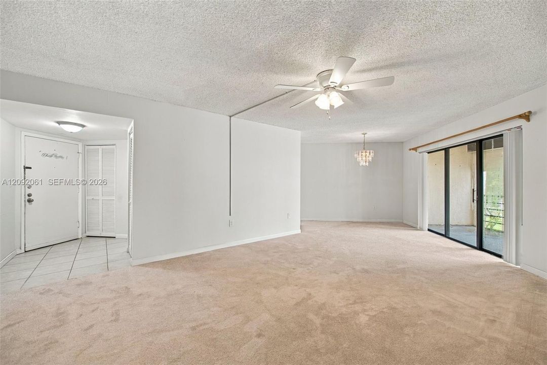 Open-concept interior featuring wall-to-wall carpeting, a ceiling fan with integrated lighting, a multi-pane glass sliding door, and a tiled entryway with louvered-door closet