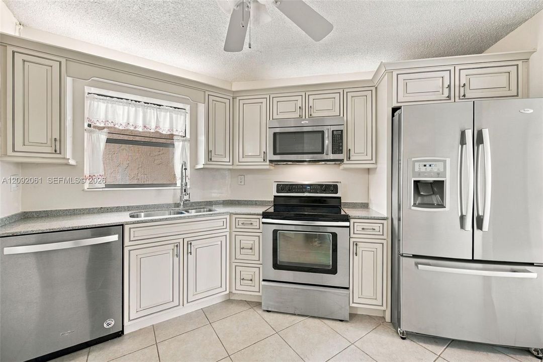 Kitchen featuring light-toned cabinetry, stainless steel appliances, speckled stone-finish countertops, and tile flooring