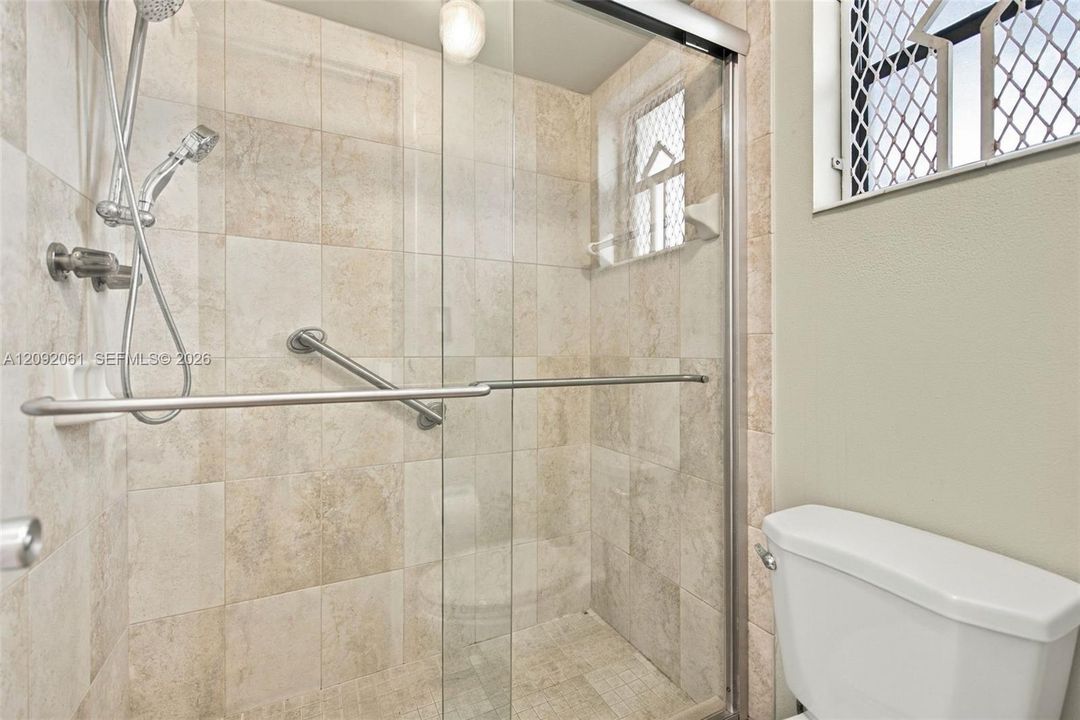 Walk-in shower enclosure with glass sliding doors, stone-finish tile surround, handheld shower fixture, and wall-mounted metal grab bar