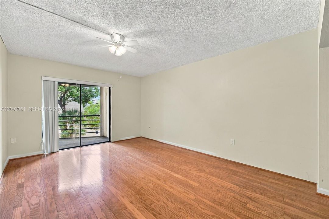 Interior space featuring wood-finish flooring, textured ceiling, ceiling fan with light fixture, and sliding glass door with access to a railed balcony