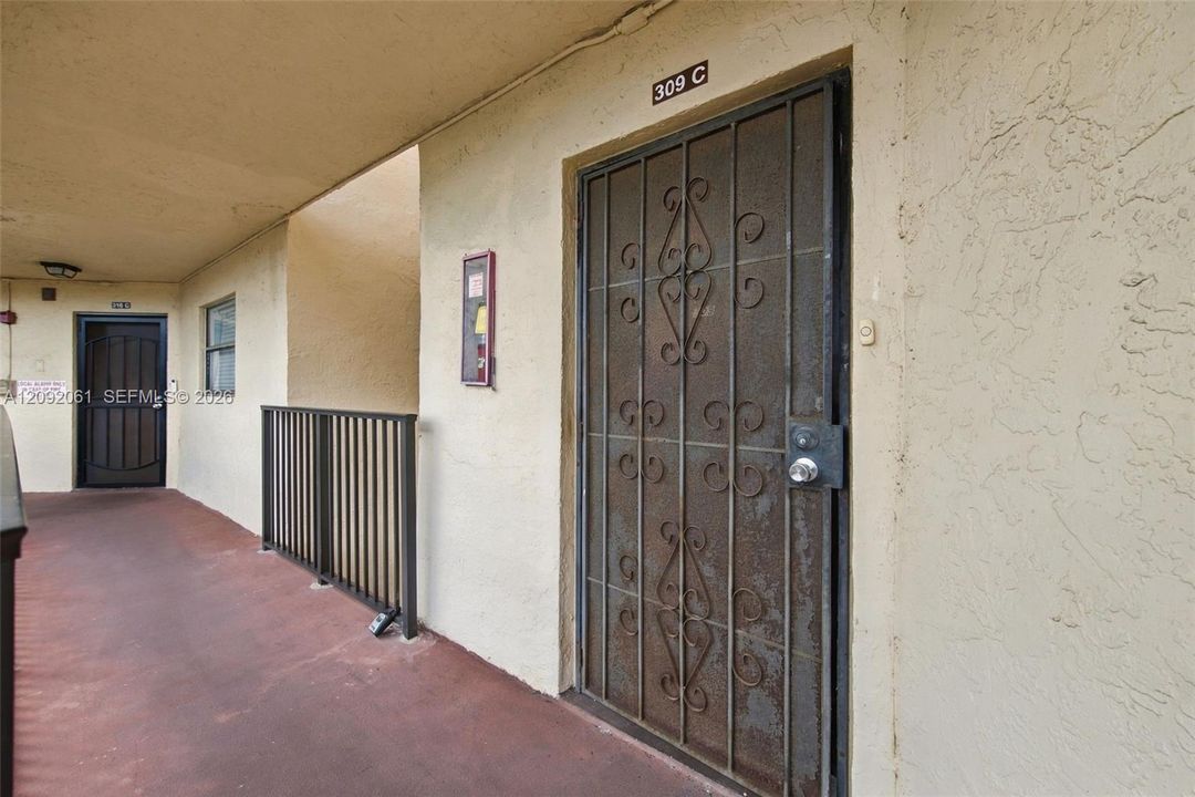 Covered exterior walkway featuring a metal security screen door with decorative scrollwork and a vertical metal balustrade