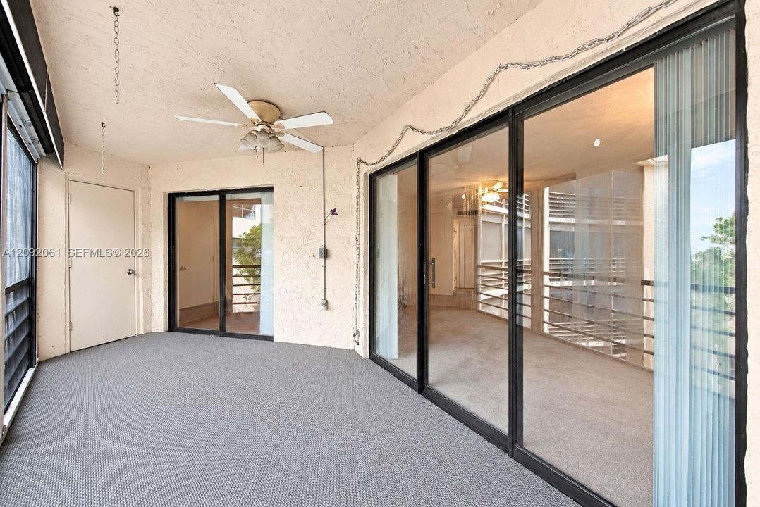 Covered balcony featuring dual sliding glass door entries, textured walls, wall-to-wall carpeting, and a ceiling-mounted fan with integrated light fixture