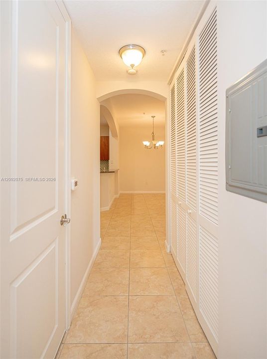 Hallway featuring square tile flooring, louvered bi-fold doors, and an arched doorway