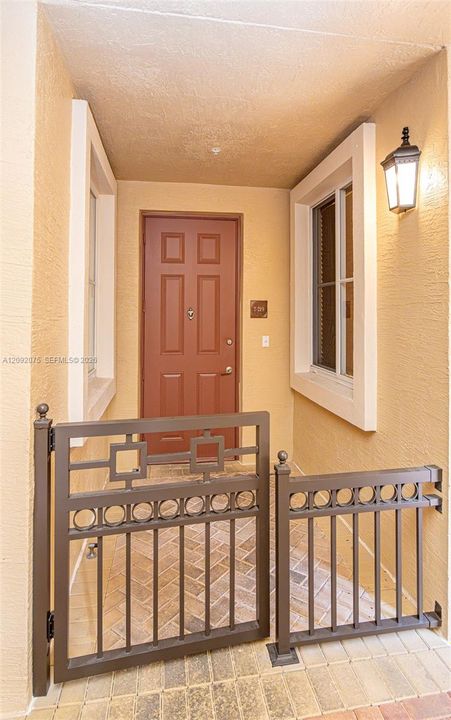 Entryway featuring a brown panel door, decorative metal gate, and brick-patterned hardscaping
