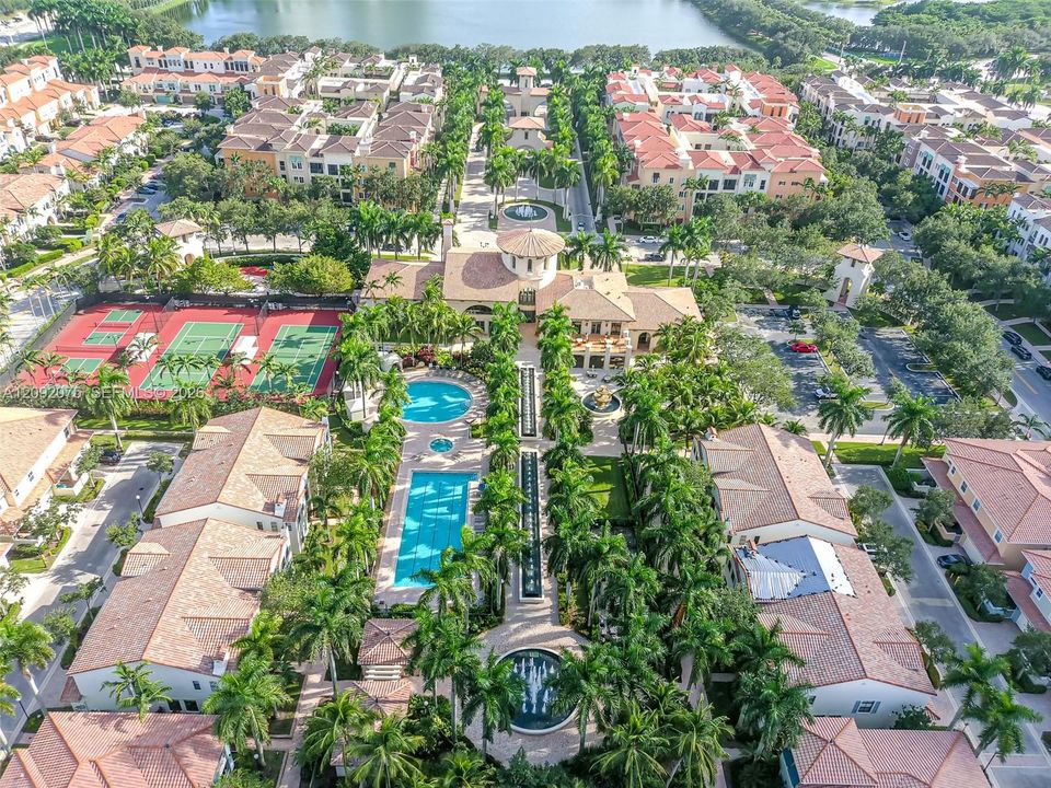 Aerial perspective featuring a central building with a rotunda, two swimming pools, multiple tennis courts, and mature palm trees