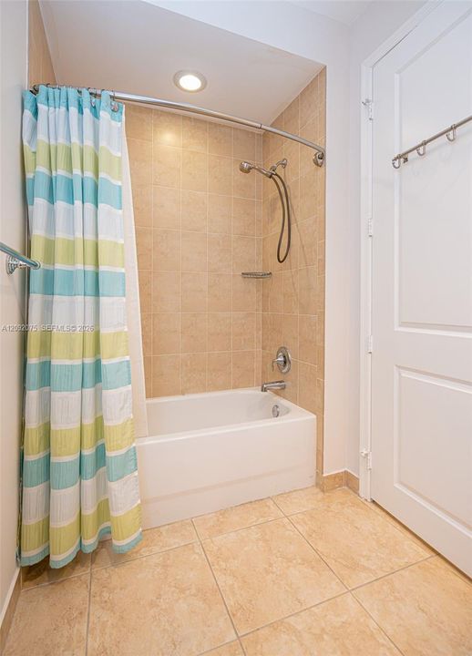 Built-in bathtub with a tile surround, curved shower rod, recessed ceiling lighting, and large format tile flooring