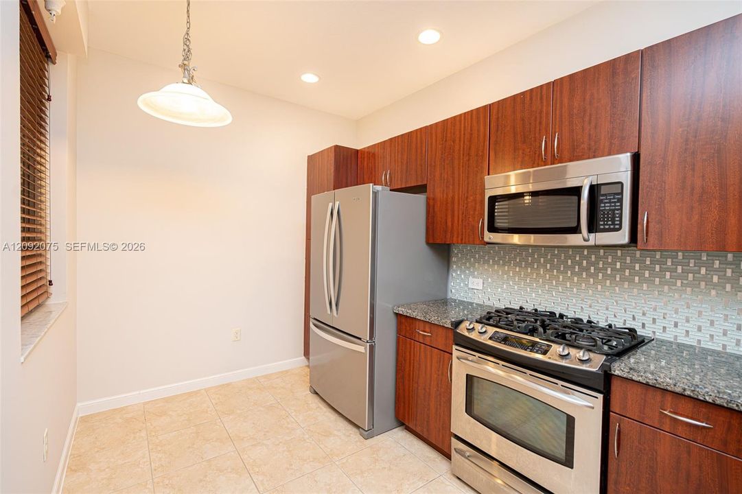 Stainless steel appliances, wood-finish cabinetry, tile flooring, glass mosaic tile backsplash, and recessed lighting