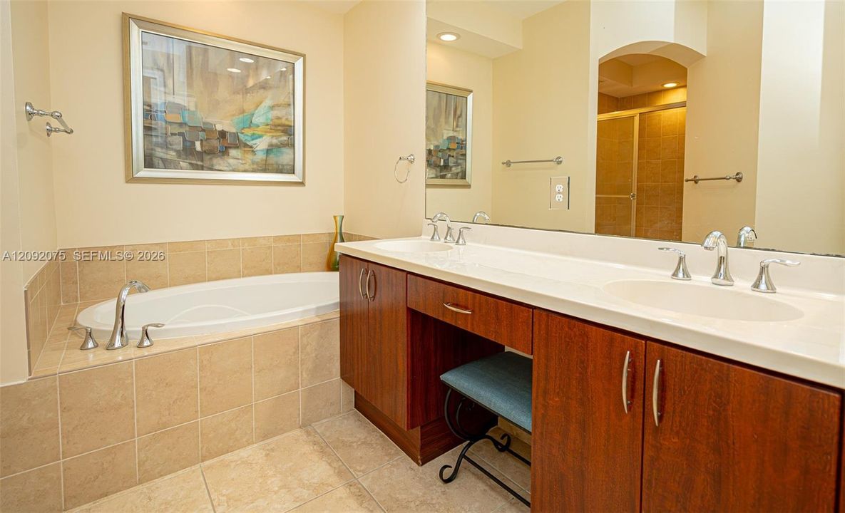 Double vanity with integrated sinks, wood-finish cabinetry, a large mirror, and a built-in soaking tub with tiled surround