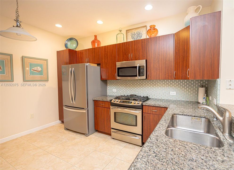 Kitchen featuring wood-finish cabinetry, stainless steel appliances, speckled stone countertops, a tile backsplash, and recessed lighting