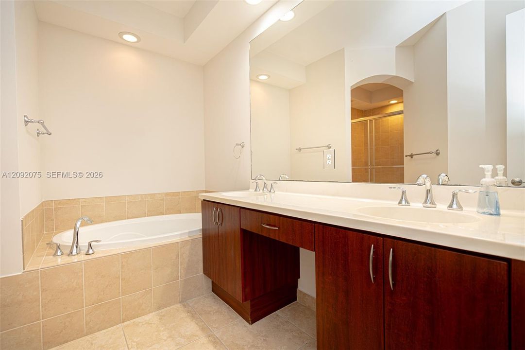 Dual vanity with integrated sinks, recessed lighting, built-in soaking tub with tile surround, and wood-finish cabinetry
