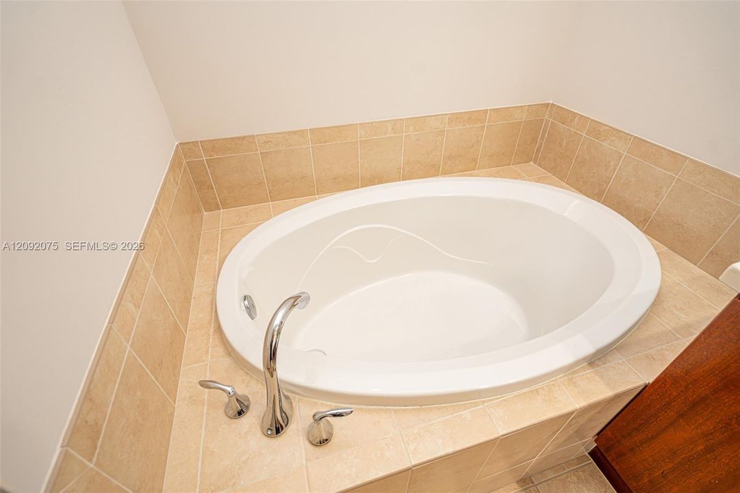 Oval drop-in bathtub with a deck-mounted chrome faucet, surrounded by neutral-toned square tile