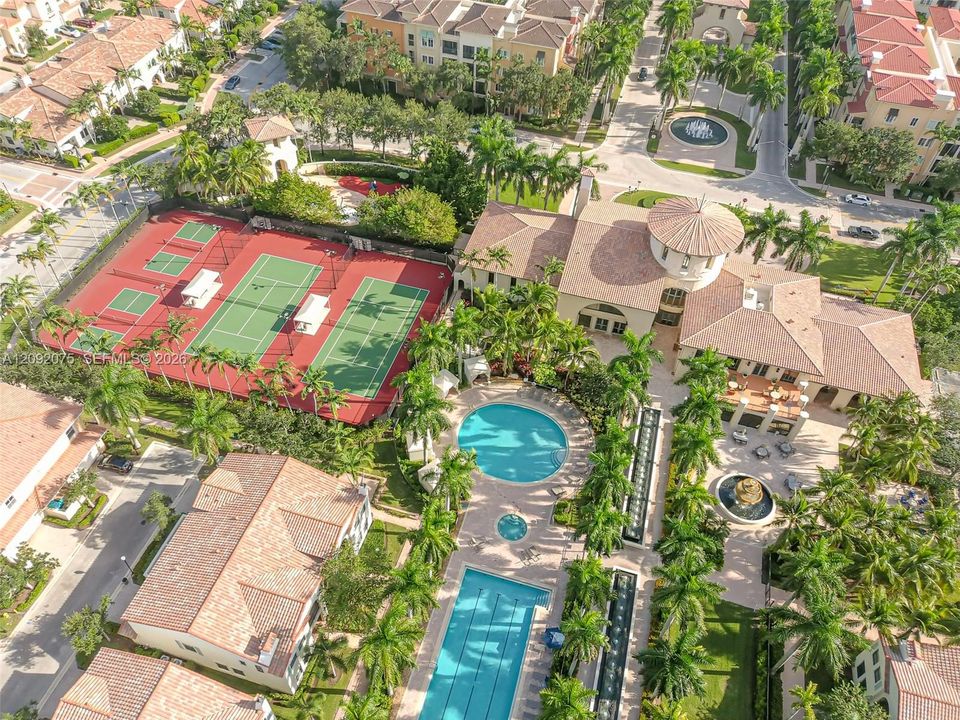 Community amenities featuring multiple tennis courts, a circular swimming pool, a rectangular swimming pool, a central clubhouse building, and mature palm tree landscaping