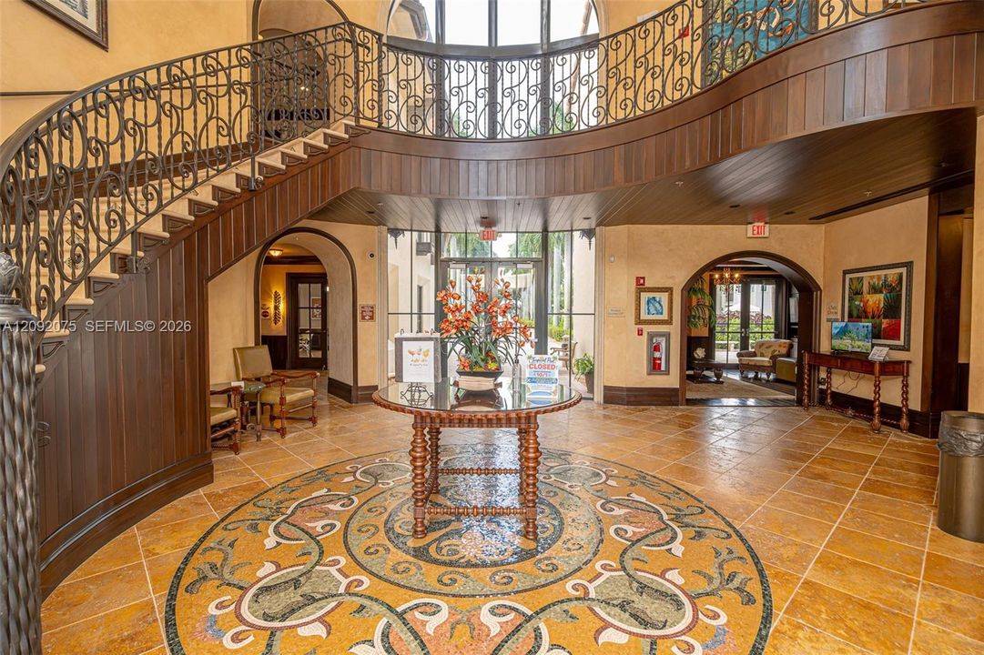 Grand foyer with a curved staircase featuring wrought iron railings, wood paneling, a detailed mosaic floor medallion, and arched doorways