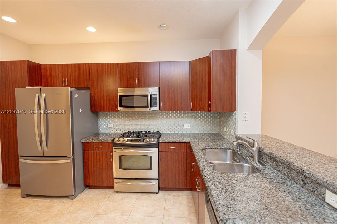 Kitchen featuring wood-finish cabinetry, stainless steel appliances, a tile backsplash, and granite countertops