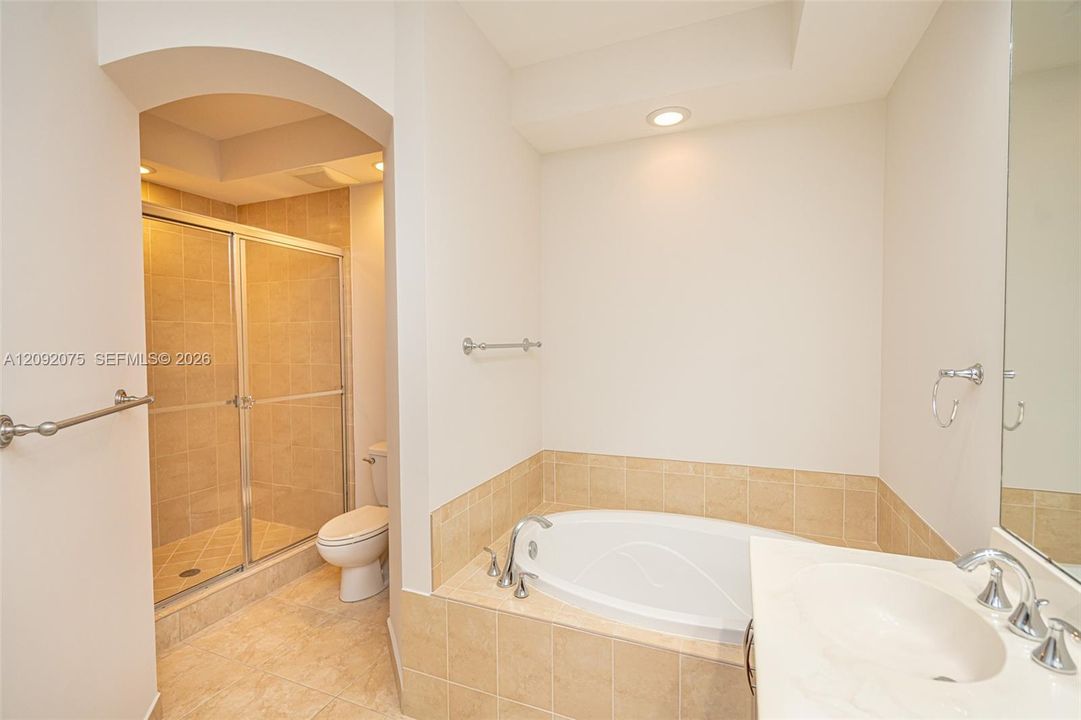 Recessed lighting, arched doorway, tile flooring, built-in bathtub, and a glass-enclosed shower
