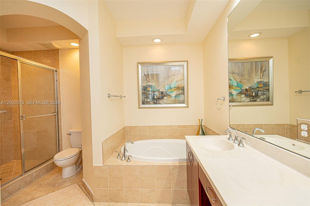 Recessed lighting, arched doorway, fully tiled shower with glass enclosure, soaking tub, and dual vanity with integrated sinks