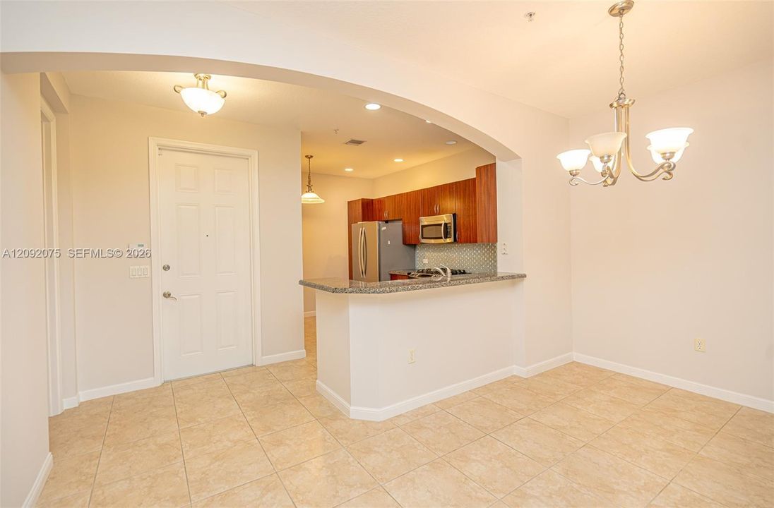 Tile flooring, arched entryway, pendant lighting, stainless steel appliances, and a breakfast bar with a stone countertop