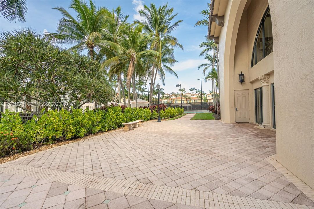 Expansive paver patio with a decorative border, surrounded by lush landscaping and mature palm trees