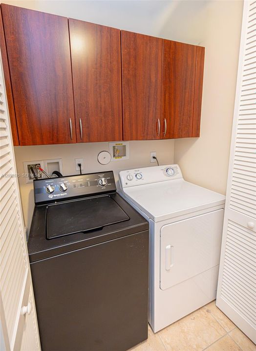 Wood-finish upper cabinetry with brushed nickel hardware, a black top-load washer, and a white front-load dryer