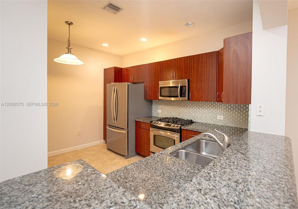 Kitchen featuring wood cabinetry, stainless steel appliances, a tile backsplash, granite countertops, and recessed lighting