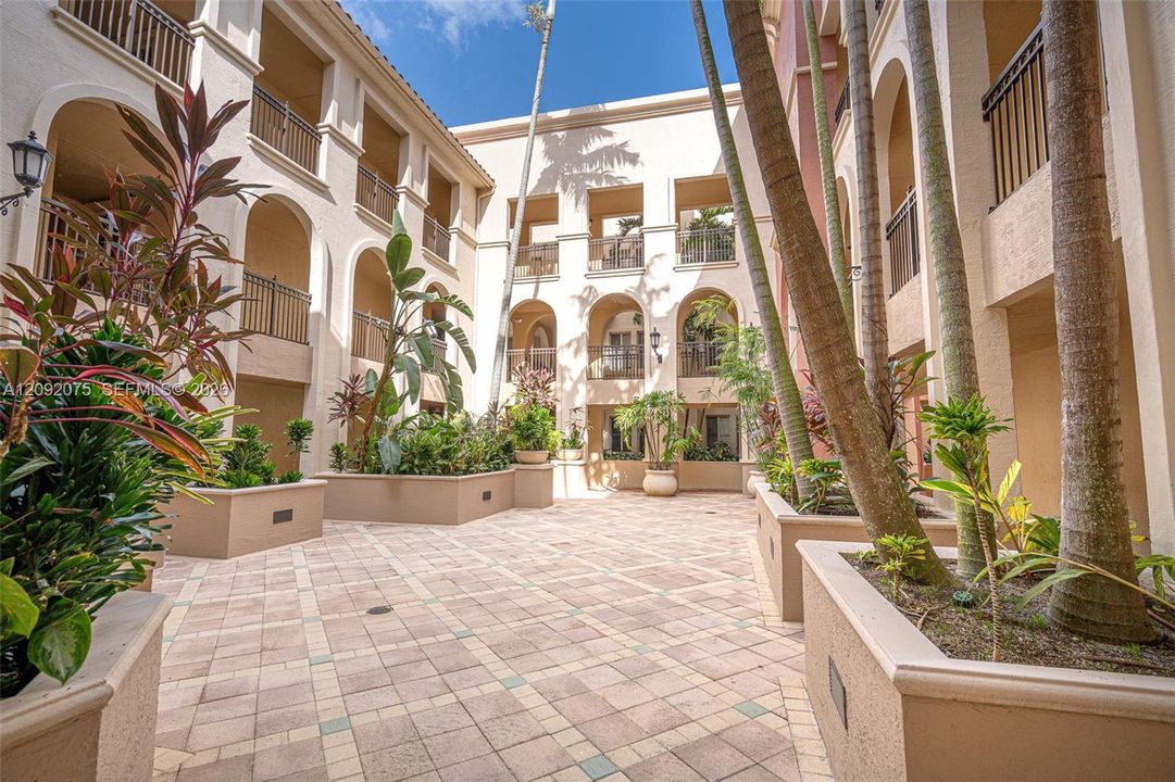Courtyard with paver flooring, multiple raised planters with mature foliage, and arched architectural details
