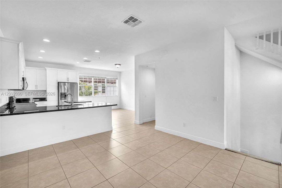 Kitchen featuring white shaker-style cabinetry, a stone countertop peninsula, stainless steel appliances, and tile flooring
