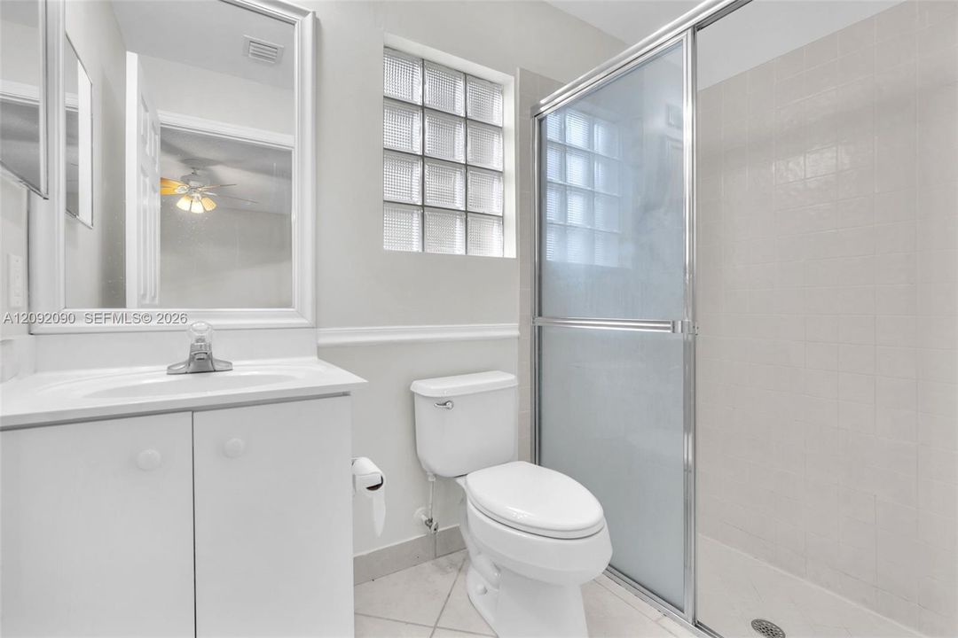 Bathroom featuring a vanity with an integrated sink, glass block window, walk-in shower with a sliding enclosure, and ceramic tile flooring