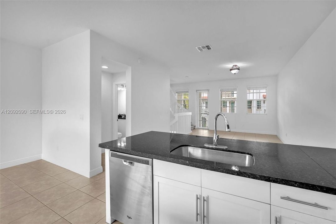 Kitchen featuring white cabinetry, dark stone-finish countertops, stainless steel undermount sink with gooseneck faucet, and stainless steel dishwasher