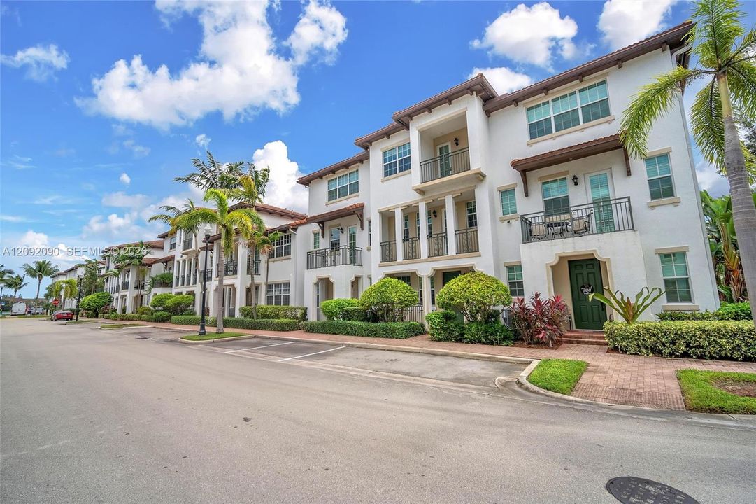 Multi-story Mediterranean-inspired exterior featuring stucco facade, recessed balconies with wrought-iron railings, decorative corbels, and brick-paver entryways
