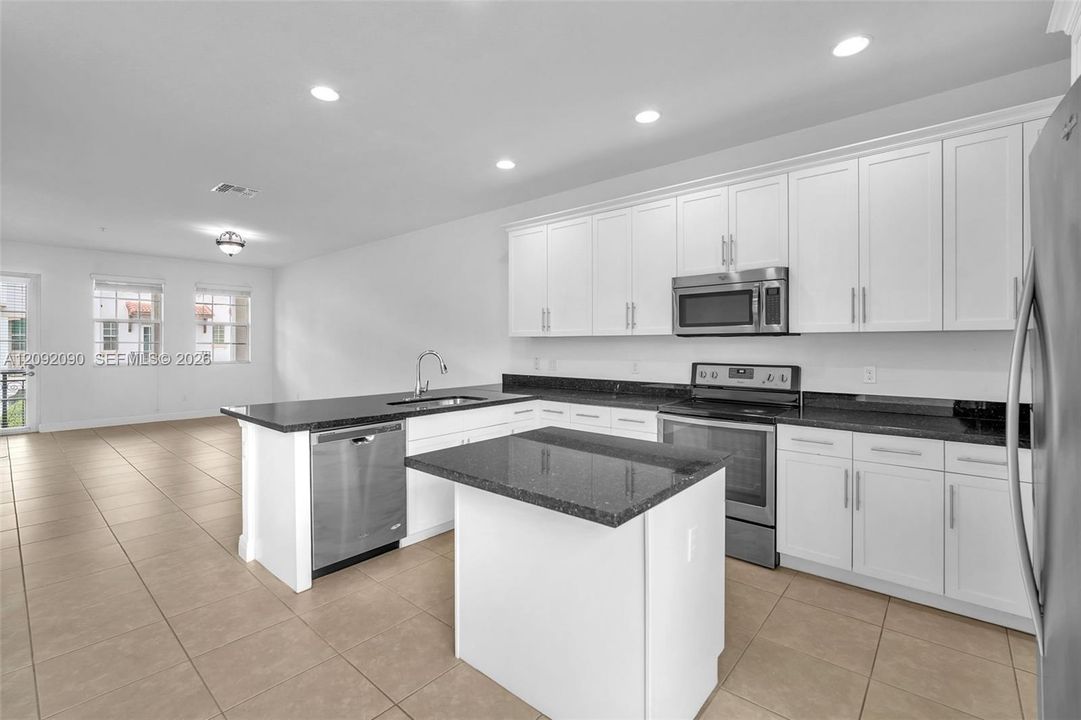 Kitchen featuring white cabinetry, dark stone countertops, stainless steel appliances, a center island, and tile flooring