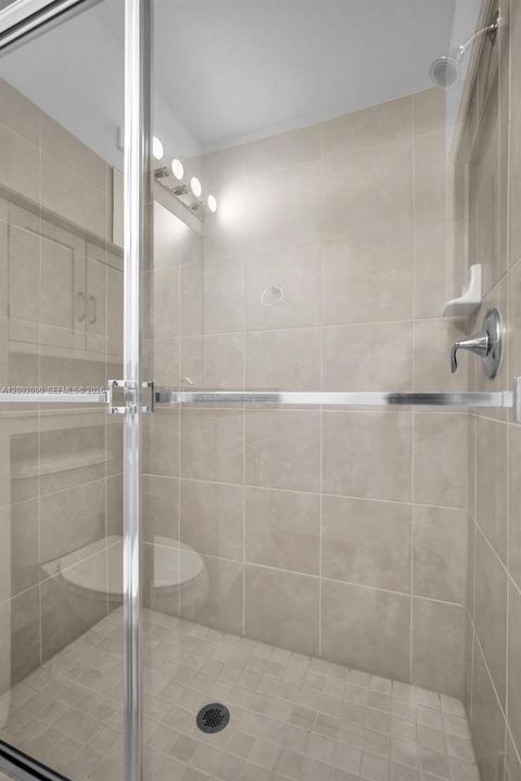 Walk-in shower featuring floor-to-ceiling neutral tile, glass enclosure with chrome hardware, built-in recessed shelf, and fixed shower head