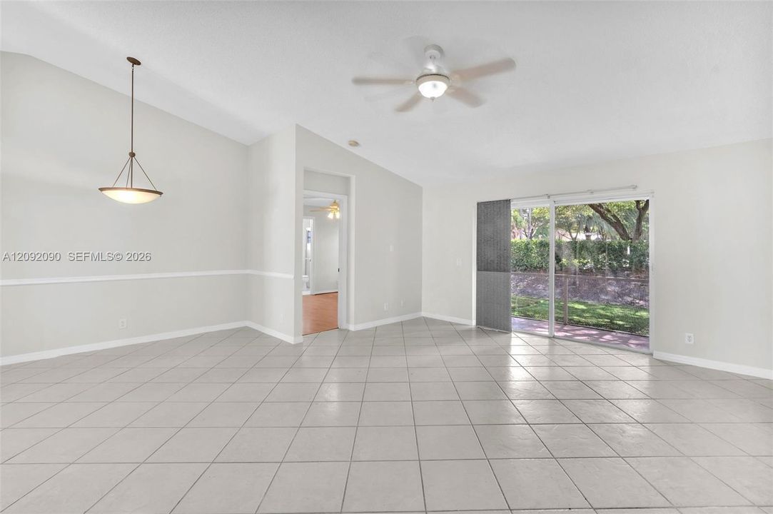 Vaulted ceilings, large-format tile flooring, a multi-light pendant fixture, a ceiling fan with integrated lighting, and sliding glass doors providing access to a patio