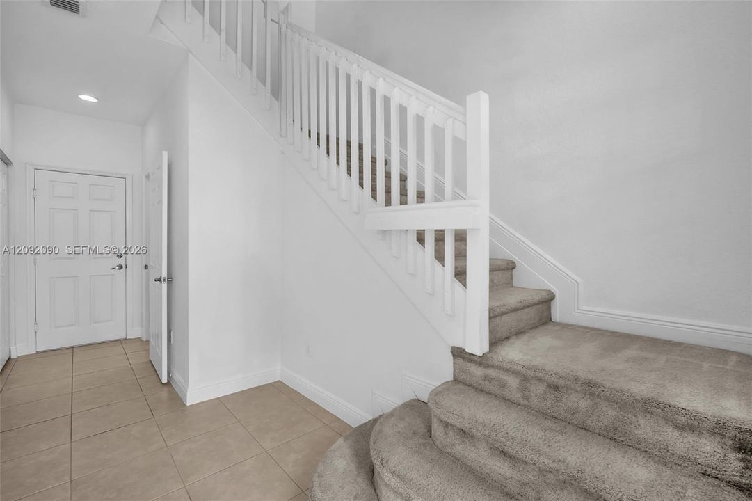 Interior foyer featuring large-format tile flooring, a recessed lighting fixture, and a staircase with carpeted treads and a painted white balustrade