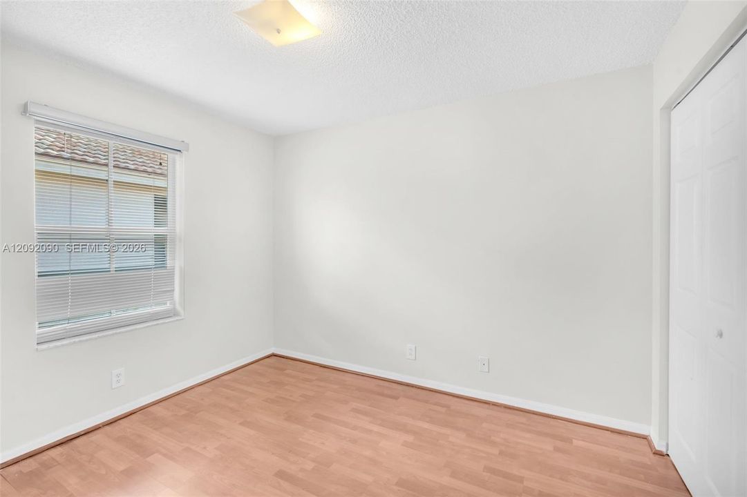 Room featuring wood-finish flooring, a neutral color palette, a window with horizontal blinds, and a built-in closet with double doors