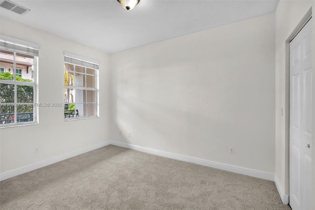 Neutral interior space featuring carpeting, two grid-patterned windows, a flush-mount ceiling light fixture, and a white interior door