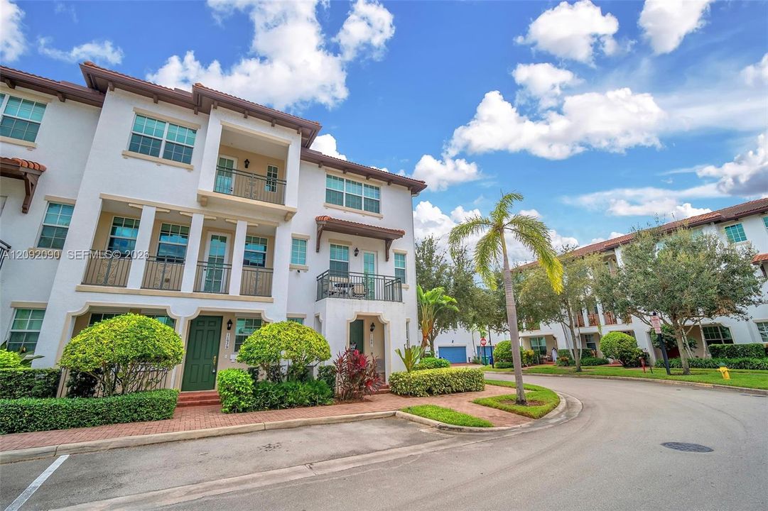 Stucco exterior featuring multi-level balconies with wrought-iron railings, arched entryway detailing, and brick-paver walkway