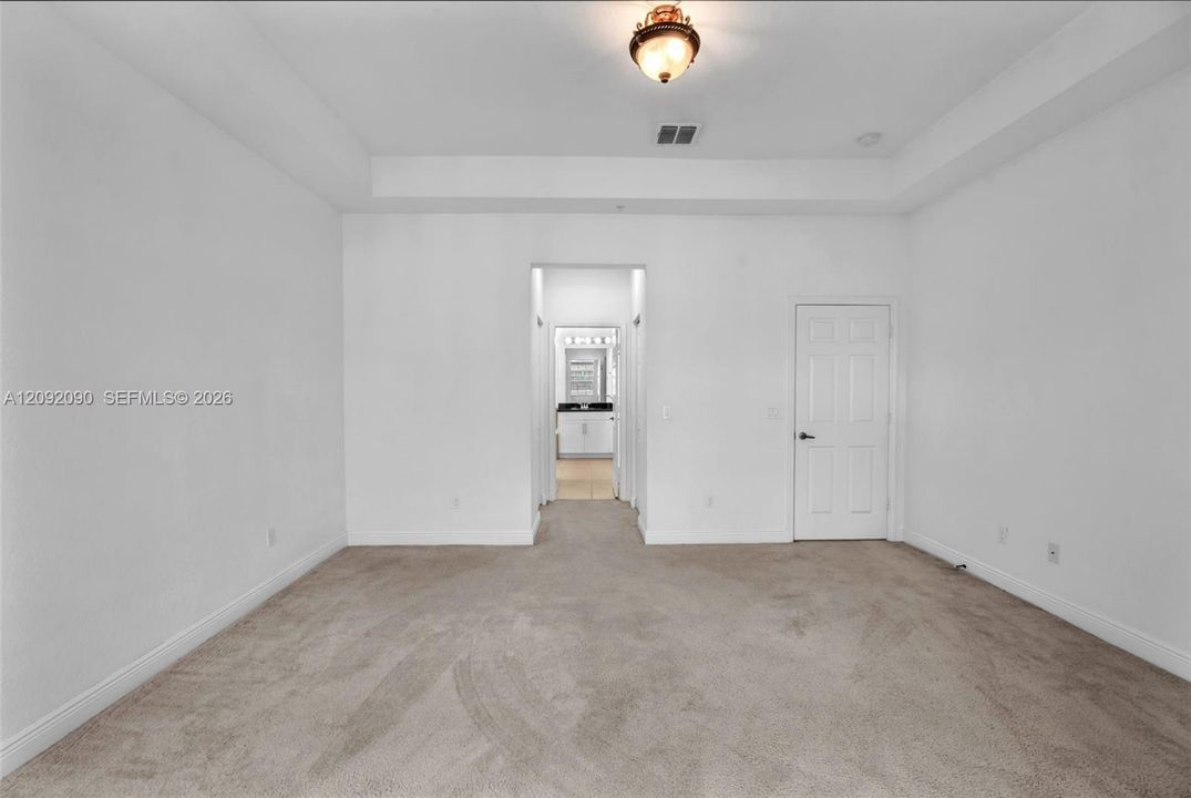 Interior space featuring a recessed tray ceiling, neutral wall-to-wall carpeting, and a flush-mount light fixture
