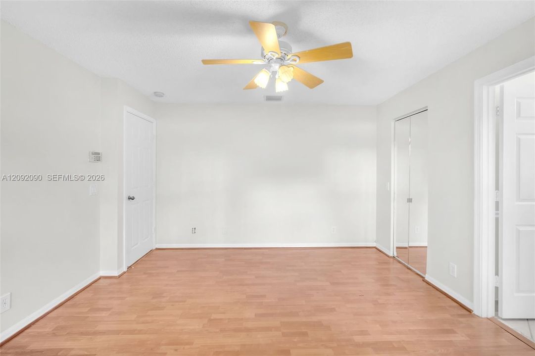 Neutral-toned interior featuring wood-finish flooring, a ceiling fan with integrated lighting, and mirrored closet doors