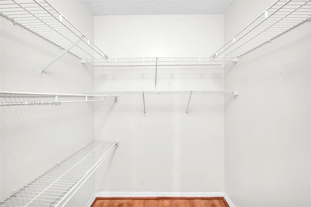 Storage area featuring multiple tiers of white wire shelving and wood-finish flooring