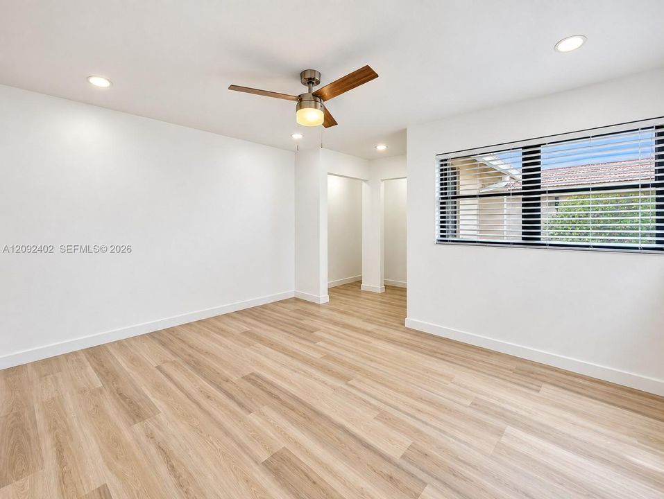 Neutral interior space featuring wood-finish flooring, recessed lighting, a modern ceiling fan with light fixture, and large windows with horizontal blinds