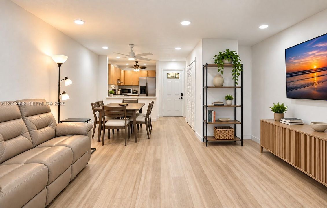 TV console & plants virtually staged for illustrative purposes.  Open-concept interior featuring light wood-finish flooring, recessed lighting, white cabinetry, and an exterior entry door with an arched glass inset